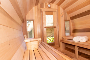 Inside the Dundalk Leisurecraft Tranquility Barrel Sauna, looking outside through the door's window, viewing towels and water bucket with ladle
