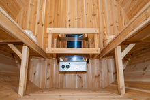 Load image into Gallery viewer, Camera view from the bottom of the floor inside the Dundalk Leisurecraft Canadian Timber Harmony Barrel Sauna viewing 6KW heater, towels on the left, benches on the left and right, and water bucket with ladle on the right